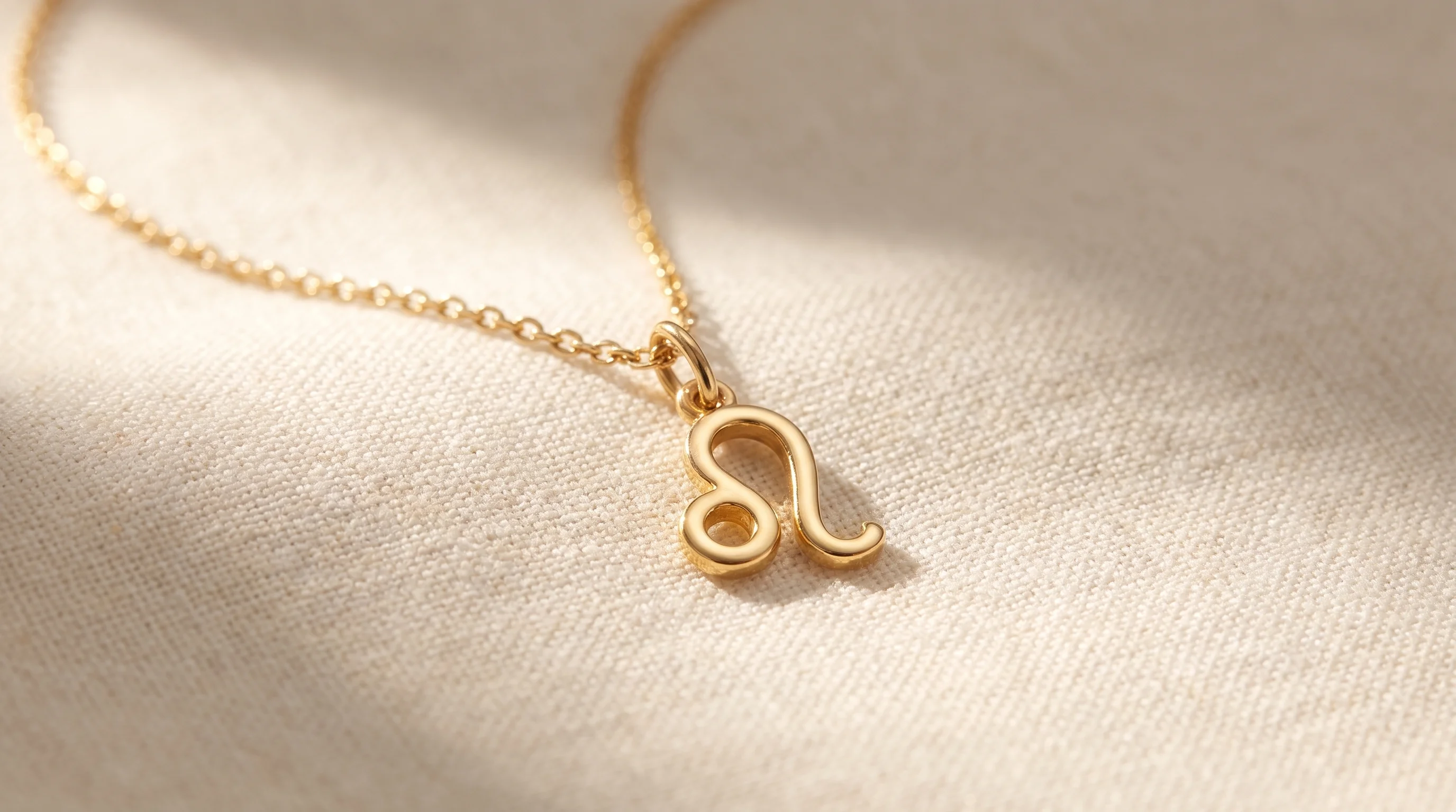 A gold Leo zodiac charm necklace resting on a cream-colored linen surface, by Enleira